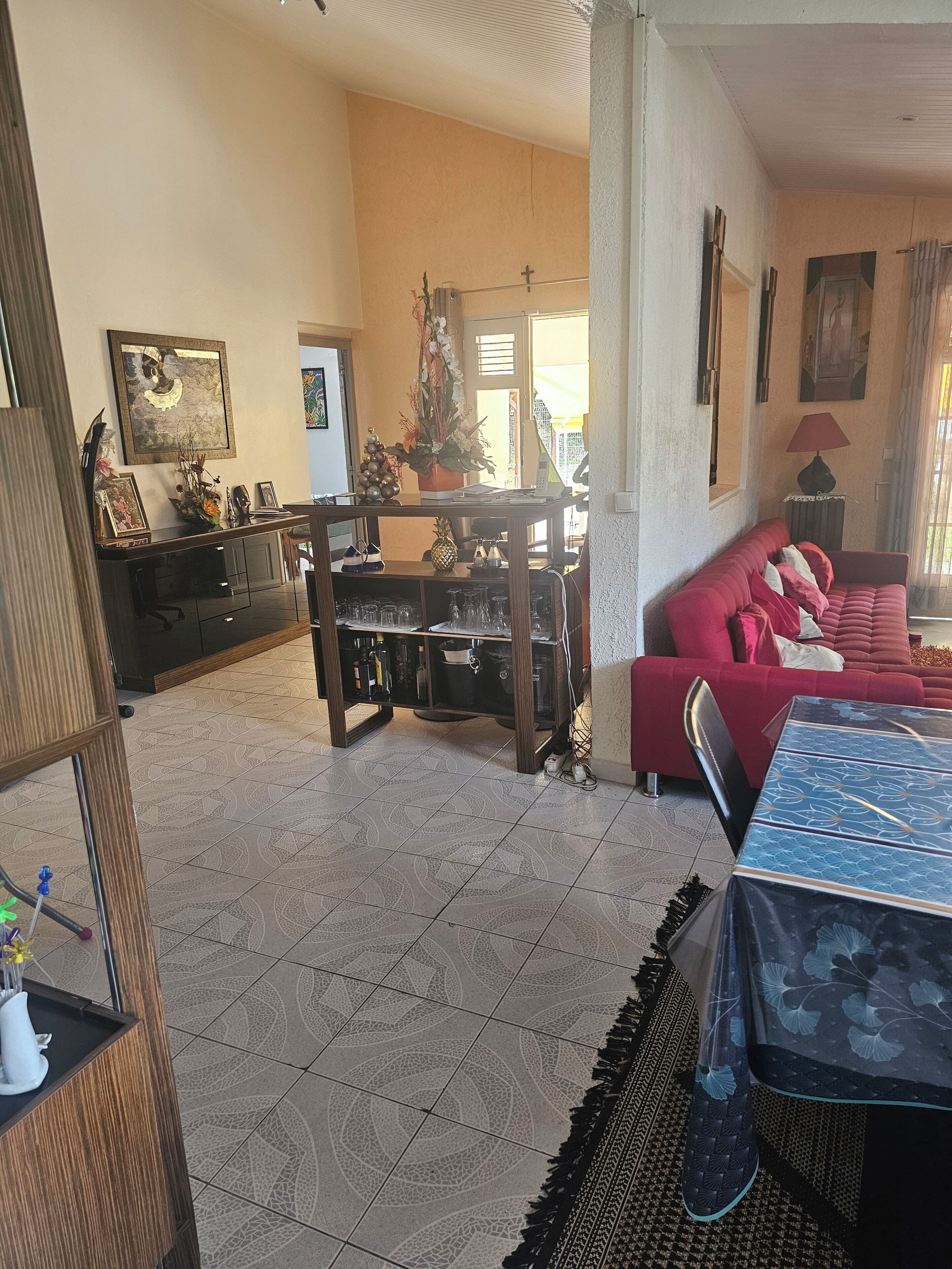 Una sala de estar con un sofá rojo, una mesa de comedor y una zona de cocina con refrigerador y armarios.
