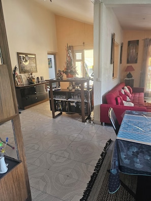 A living room with a red sofa, a dining table, and a kitchen area with a refrigerator and cabinets.