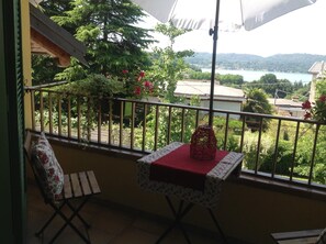 A balcony with a table and chair, a view of a lake, and surrounding greenery. - At the number in Viverone (Viverone)