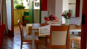 Un coin repas avec une table dressée pour deux personnes, un saladier rempli de fruits et un vase avec des fleurs.