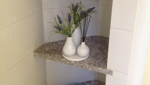 Une salle de bain avec des murs carrelés de carreaux blancs, un comptoir en granit et une étagère sur laquelle est pliée une serviette.