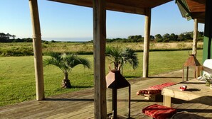 A wooden deck with a table and benches, palm trees, and a view of a grassy field and distant trees. - Beach House facing the sea in dreaming Estancia (Punta del Este)