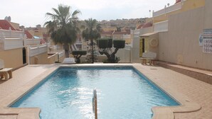 A swimming pool with a metal safety rail, palm trees, and a tiled deck. - Apartment for rent 5-6 people, Costa Blanca, Orihuela Costa Spain (Orihuela)