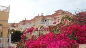 A yellow building with a red roof, white balconies, and pink flowers in the foreground. - Apartment for rent 5-6 people, Costa Blanca, Orihuela Costa Spain (Orihuela)