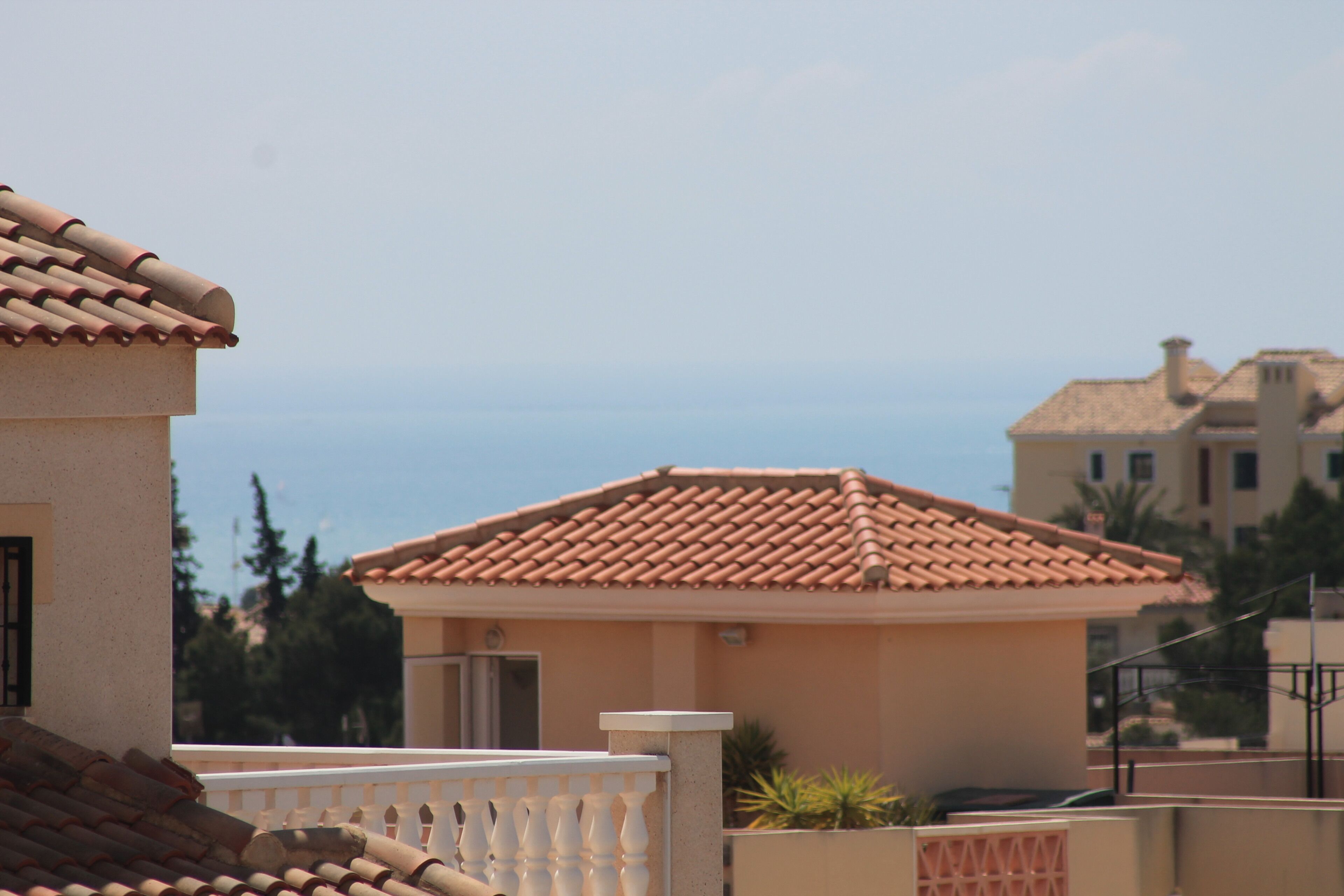 Un immeuble résidentiel avec un toit recouvert de tuiles, un balcon blanc et une vue sur la mer.