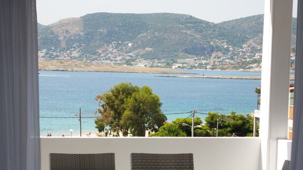 A balcony with wicker chairs overlooking a coastal view with houses and hills.