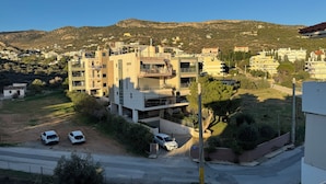 A modern apartment building with a flat roof, multiple balconies, and a parking area with three cars.