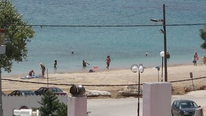 A beach with people swimming and sunbathing, cars parked nearby, and a clear view of the sea.