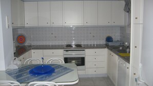 A compact kitchen with white cabinets, a gas stove, a sink, and a dining table with chairs.