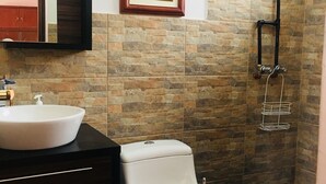 A bathroom with a white toilet, a white sink, a framed picture on the wall, and a shower area with a black hose. - Apartment in Historic Downtown Quito (Quito)