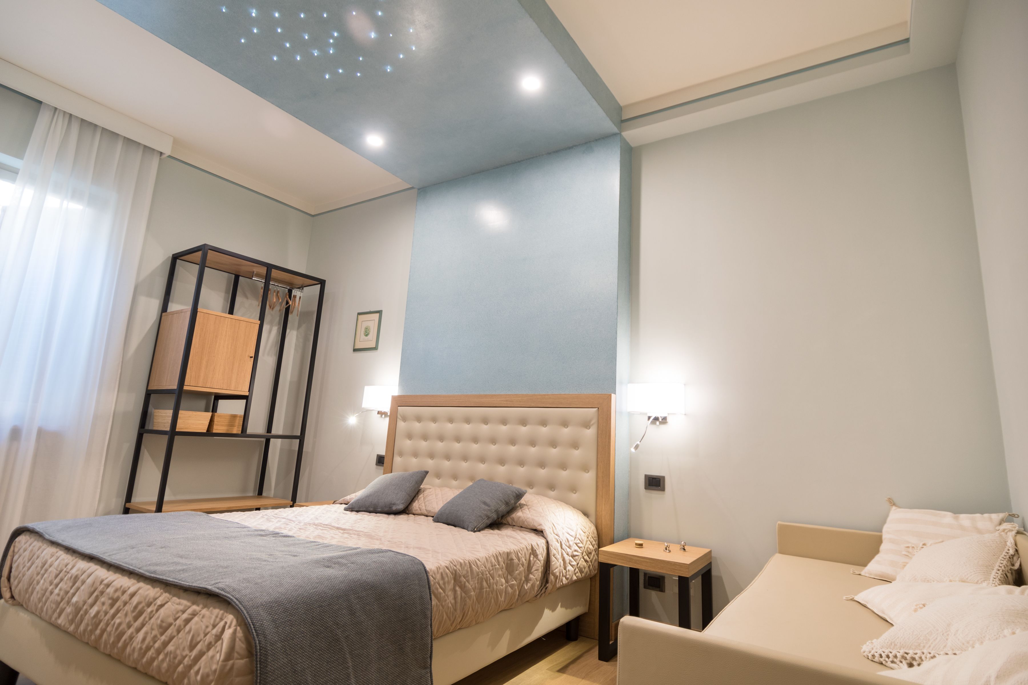 Une chambre à coucher comprenant un grand lit, un lit plus petit, une table de chevet, une armoire en bois et un luminaire fixé au plafond.