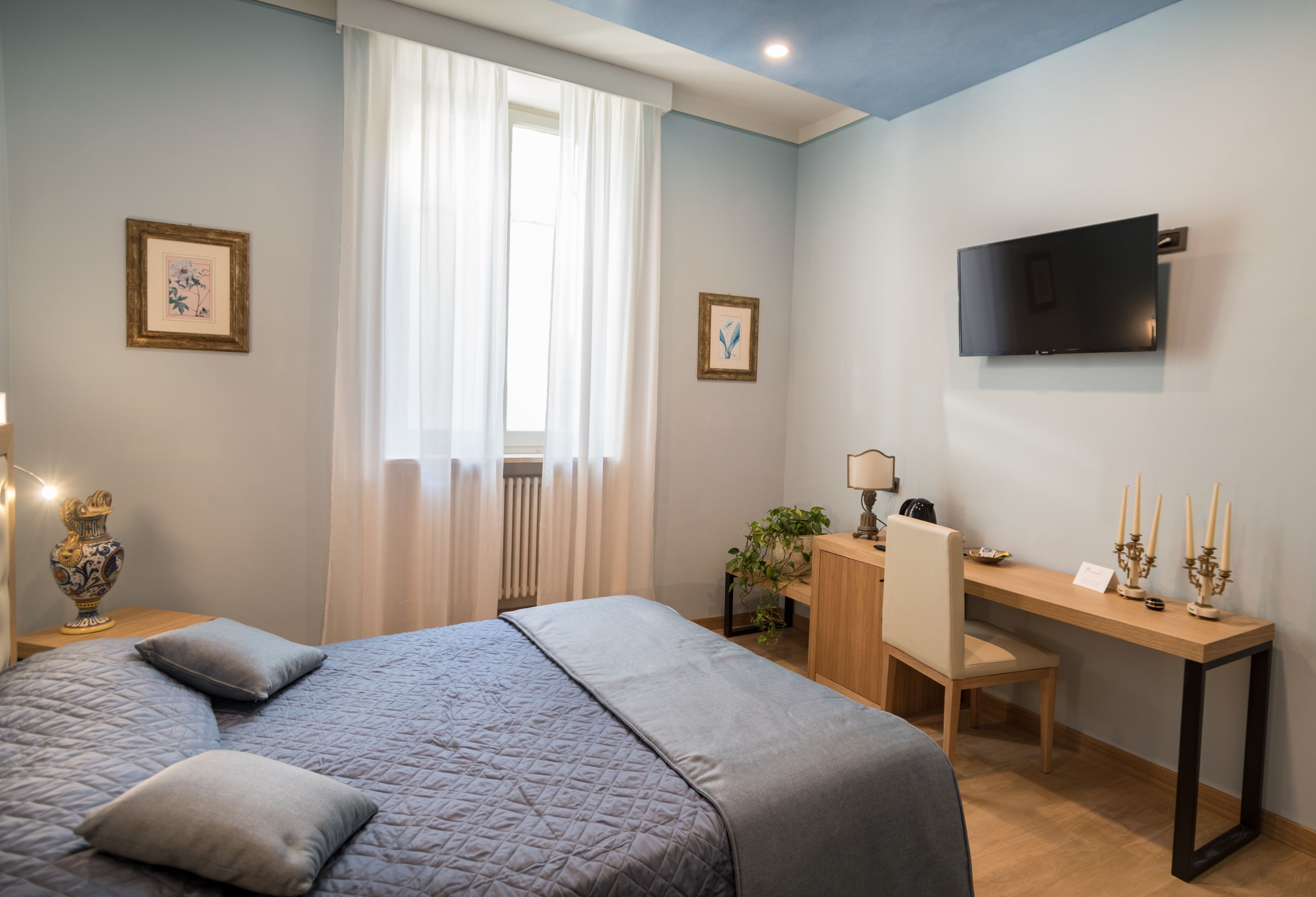 Un dormitorio con una cama, un escritorio, una silla, un televisor y dos cuadros en la pared.