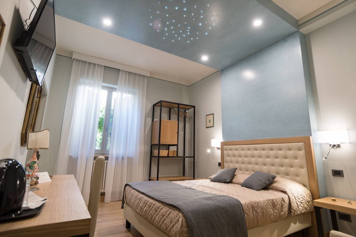 A neatly arranged bedroom with a bed, bedside table, and a desk with a chair.