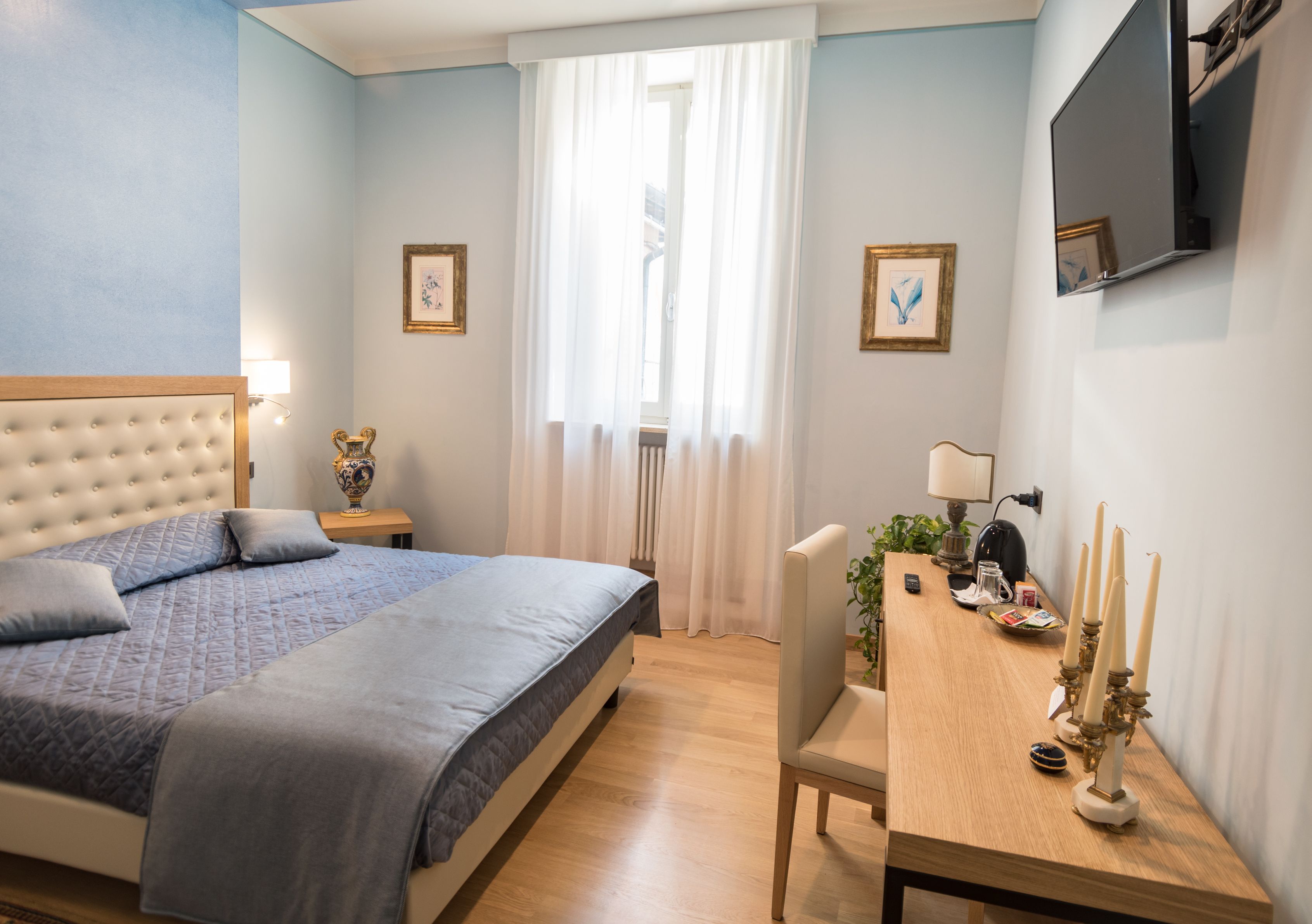 Un dormitorio con cama, mesita de noche, lámpara y televisor montado en la pared.