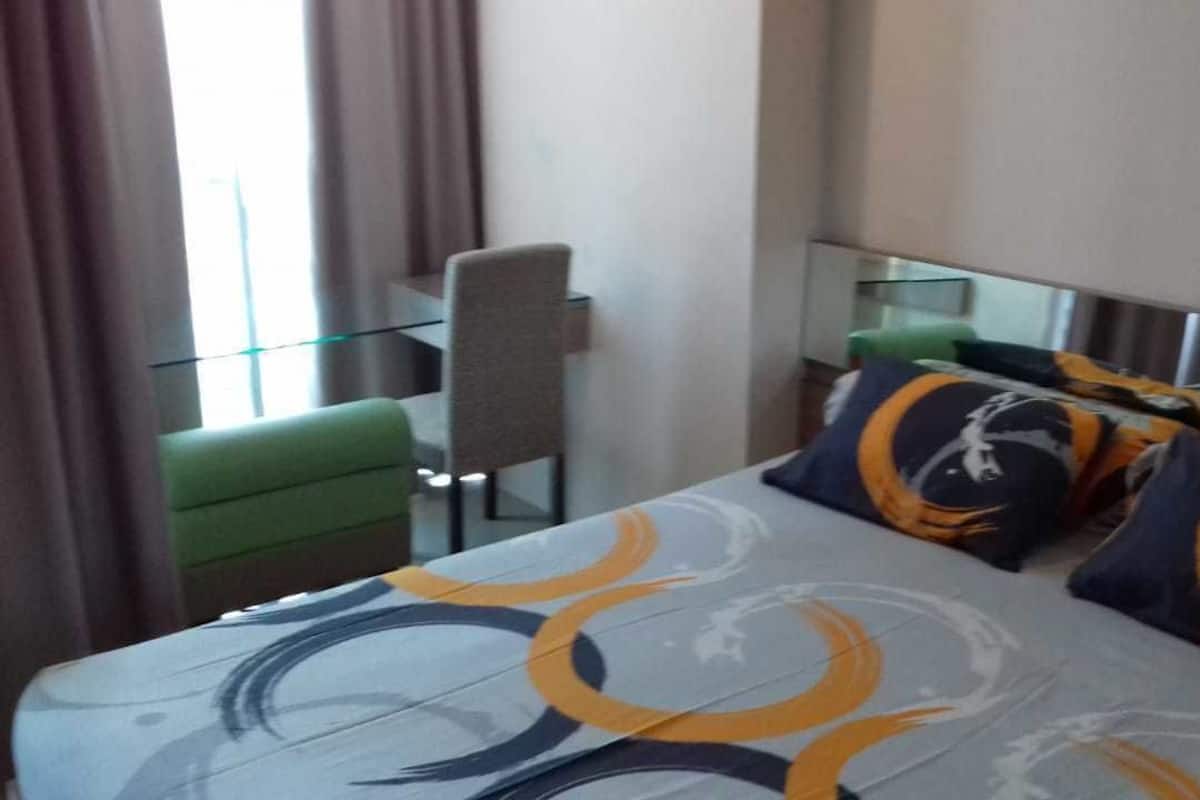 A hotel room with a bed, green armchair, and a glass table.