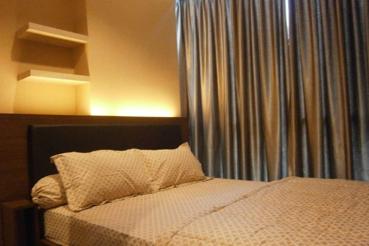 A hotel room with a bed, a headboard, and a window with curtains.