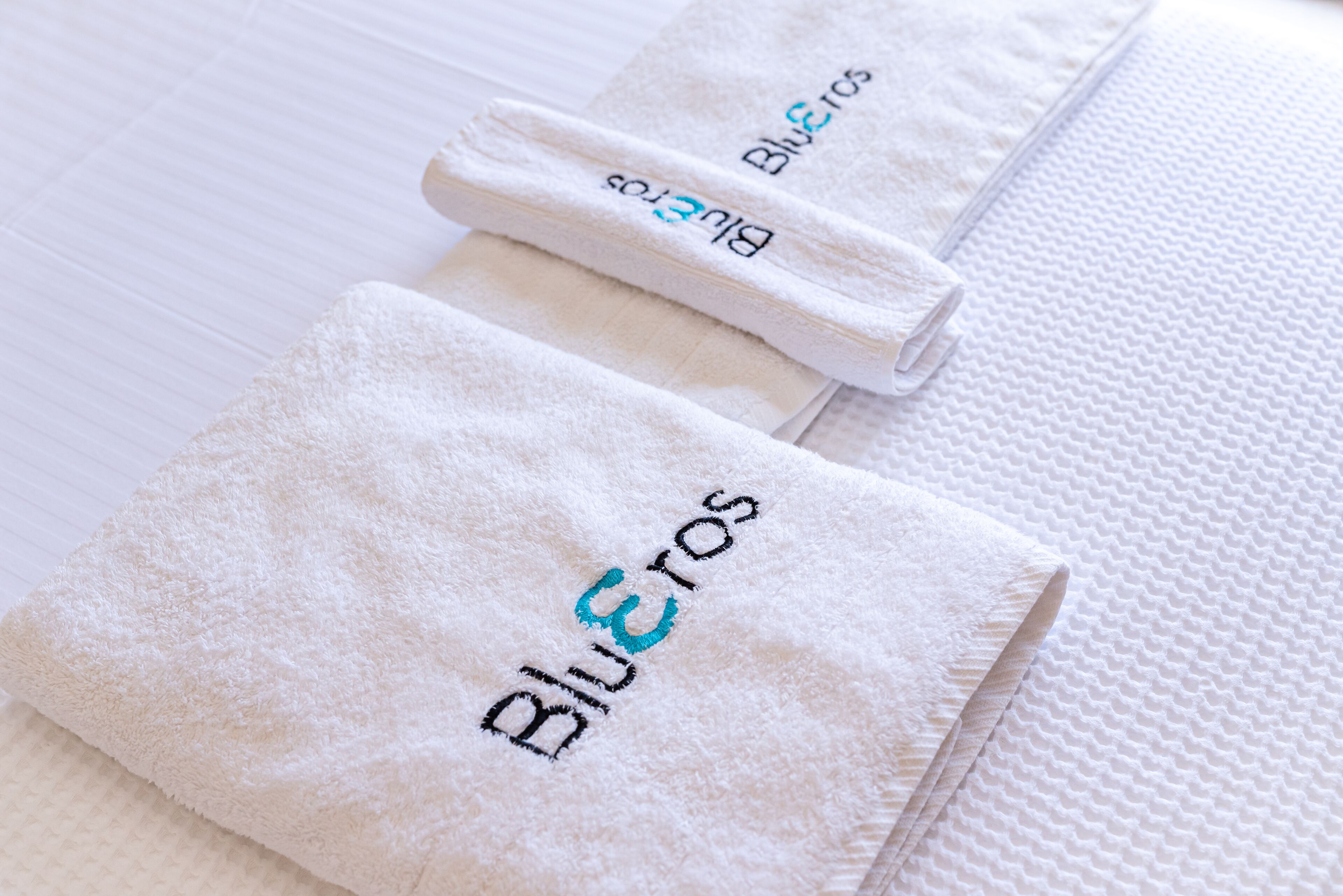 Neatly folded white towels with embroidered text, placed on a textured surface.