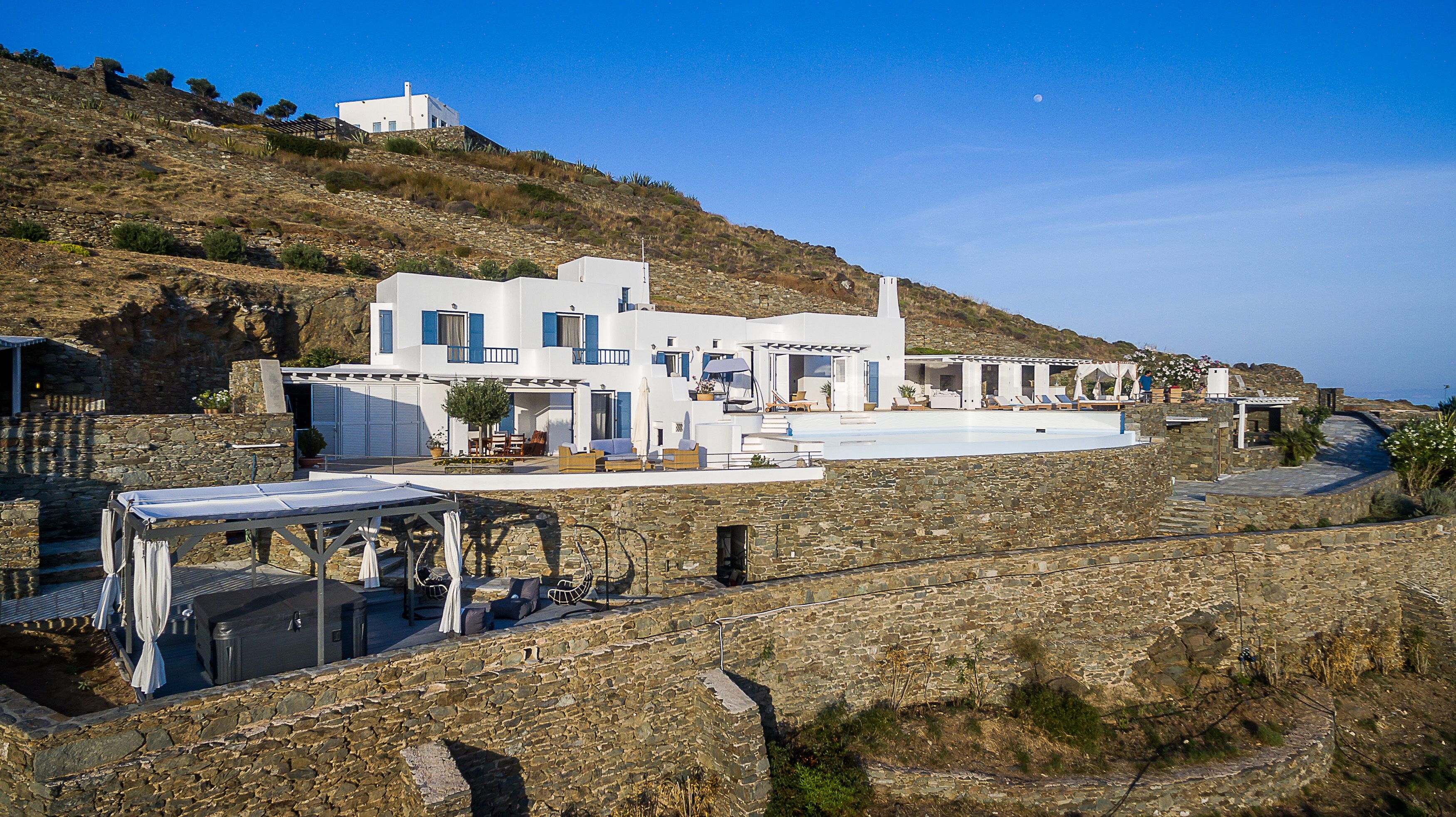 A white villa with a pool, stone walls, and a view of the sea.