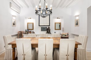 A dining room with a wooden table, white upholstered chairs, a chandelier, and wall-mounted artwork. - The perfect hideaway in the Greek blue Aegean seas (Syros Cyclades)