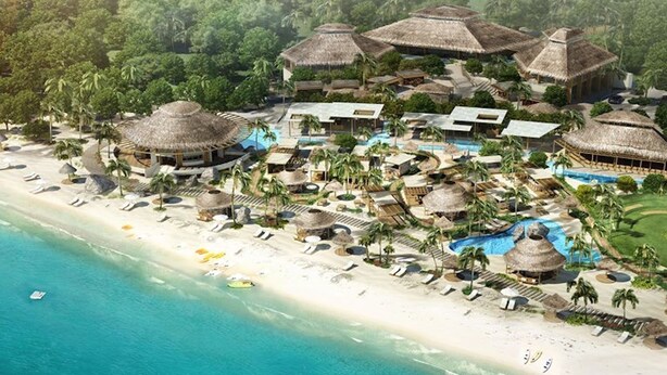 Un resort con varias estructuras de techo de paja, una gran piscina y una playa con tumbonas.
