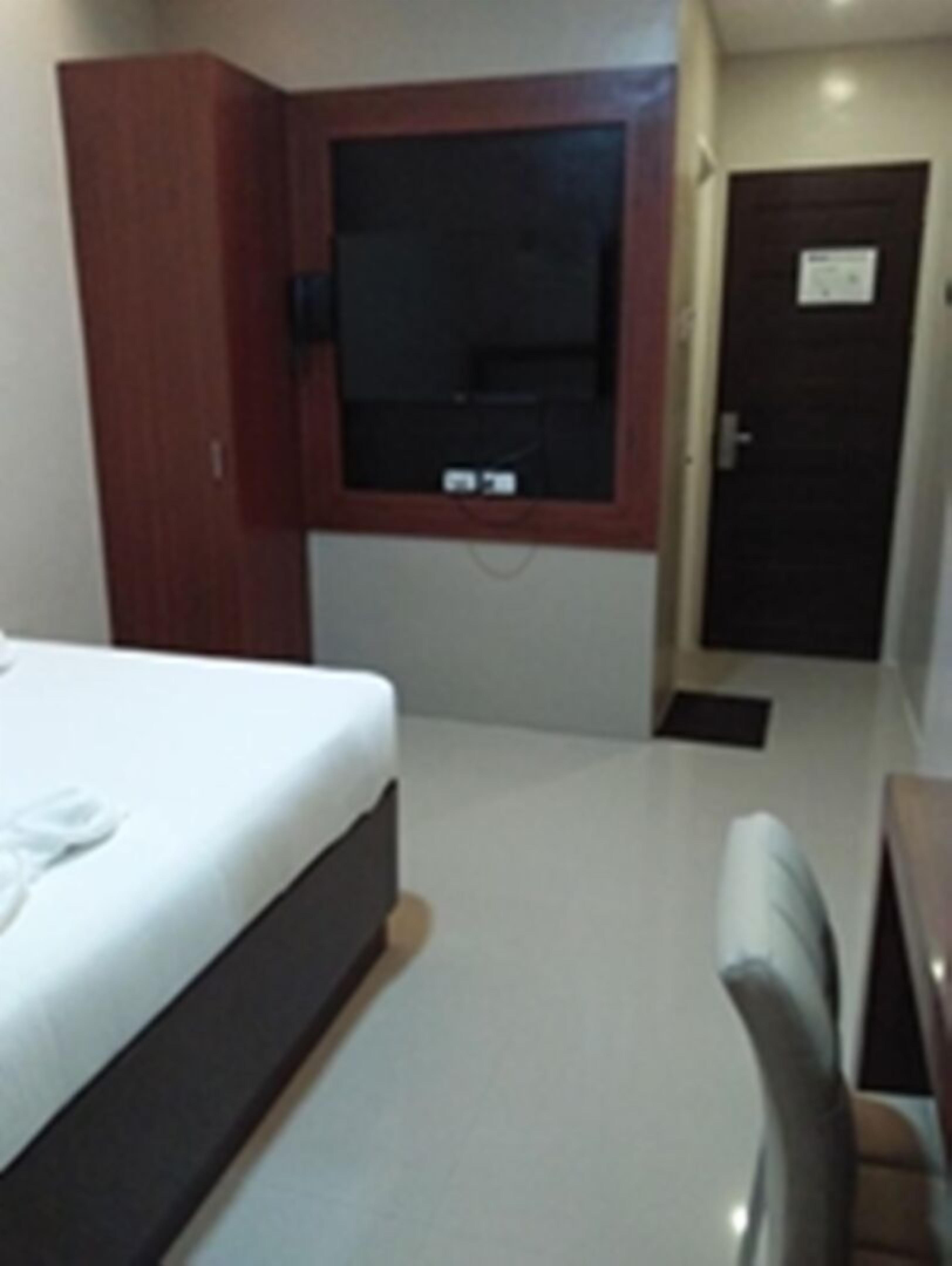 A hotel room with a bed, a TV, a desk, and a door.