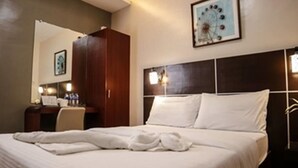 Une chambre d’hôtel avec un grand lit, une armoire en bois, un bureau avec une chaise et un luminaire fixé au mur.