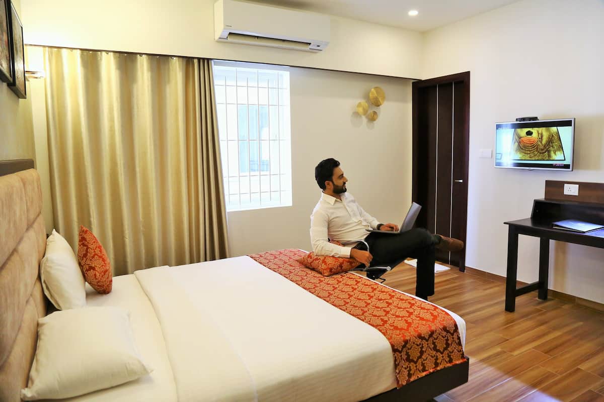 A hotel room with a bed, a desk, a television, and an air conditioning unit.