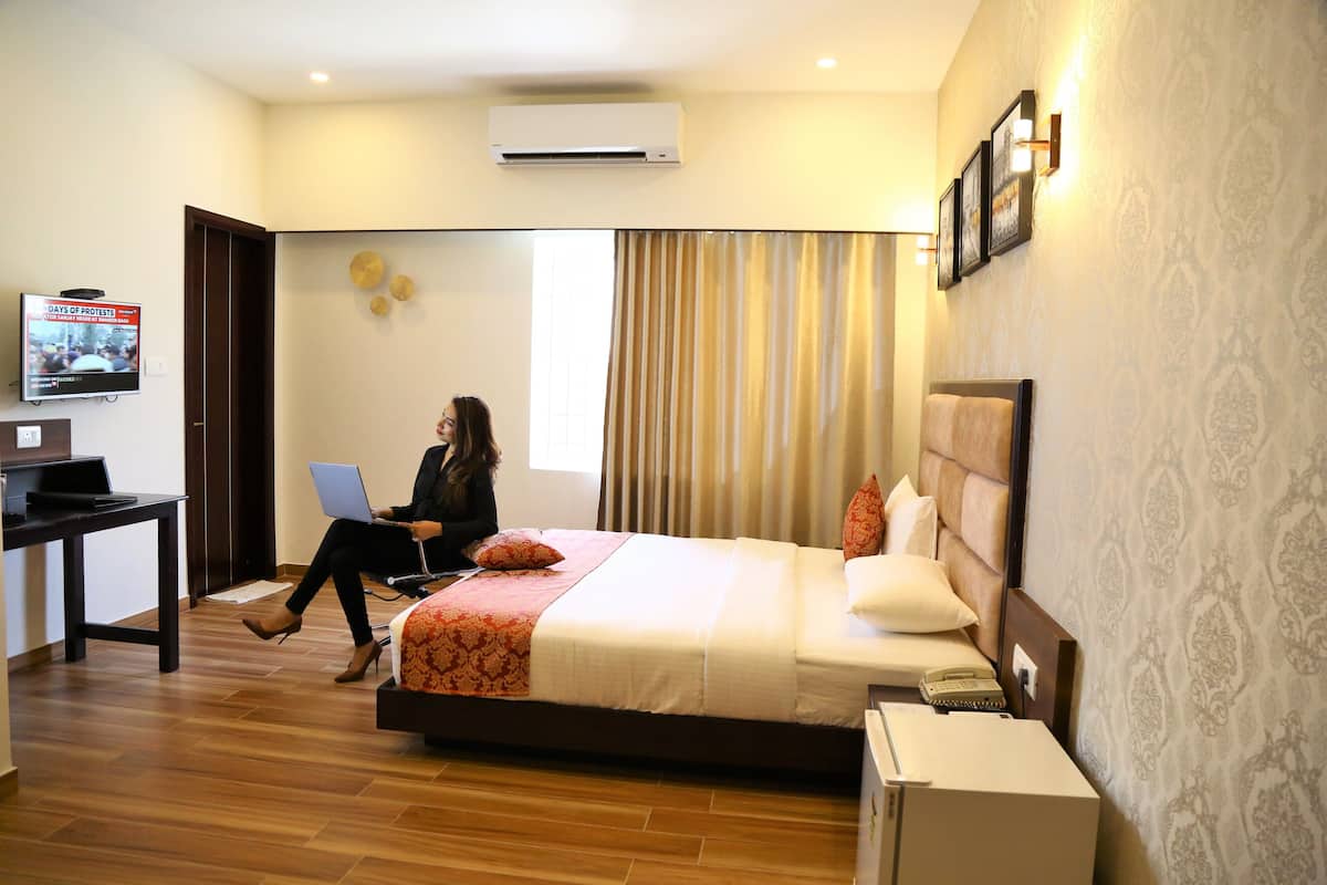 A hotel room with a bed, a desk with a laptop, a television, and an air conditioner.
