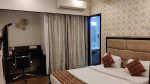 Habitación de hotel con cama, escritorio, silla y baño visible a través de una puerta abierta.