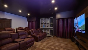 Un cine en casa con sillones reclinables de cuero, piso de madera, una estantería y una pantalla grande mostrando la Torre Eiffel.