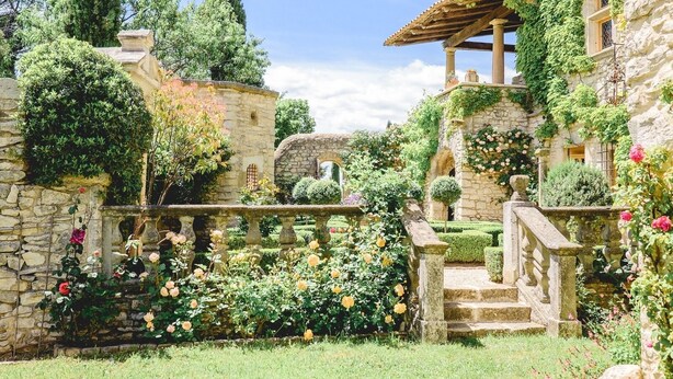 Un jardin avec des murs en pierre, une pergola en bois et un escalier en pierre.