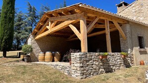 Il s’agit d’un bâtiment rustique en pierre, surmonté d’une pergola en bois qui abrite un espace couvert. Les murs et les fondations sont également en pierre.