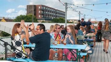 A rooftop bar with outdoor seating, a view of a modern building, and string lights.