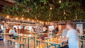 Un amplio comedor interior con mesas y bancos de madera, plantas colgantes e iluminación ambiental.