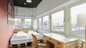 Una habitación con dos camas, un escritorio de madera y amplios ventanales con vistas a la ciudad.