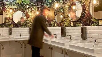 Een openbaar toilet met drie wasbakken, spiegels en een decoratieve wand met bladmotieven.