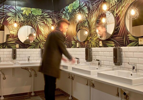 A public restroom with three sinks, mirrors, and a decorative wall with leaf patterns.