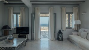 A modern living room with a television, sofa, and a view of the sea through large windows. - TERRA retreat in Paros, with prIvate pool, stunning sea view, near sandy beaches (PARIKIA PAROS)