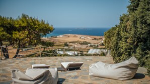 A stone-tiled terrace with lounge chairs and a view of the sea. - TERRA retreat in Paros, with prIvate pool, stunning sea view, near sandy beaches (PARIKIA PAROS)