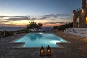 Une piscine rectangulaire avec une terrasse en pierre, deux lanternes et une structure en pierre ornée d’arches.