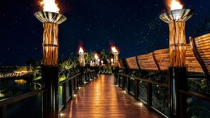 A wooden deck with torches, surrounded by a railing and palm trees, under a starry night sky. - Stunning Grand Luxxe 2-Bedroom Loft, Perfect for you to indulge in paradise. (Nuevo Vallarta)