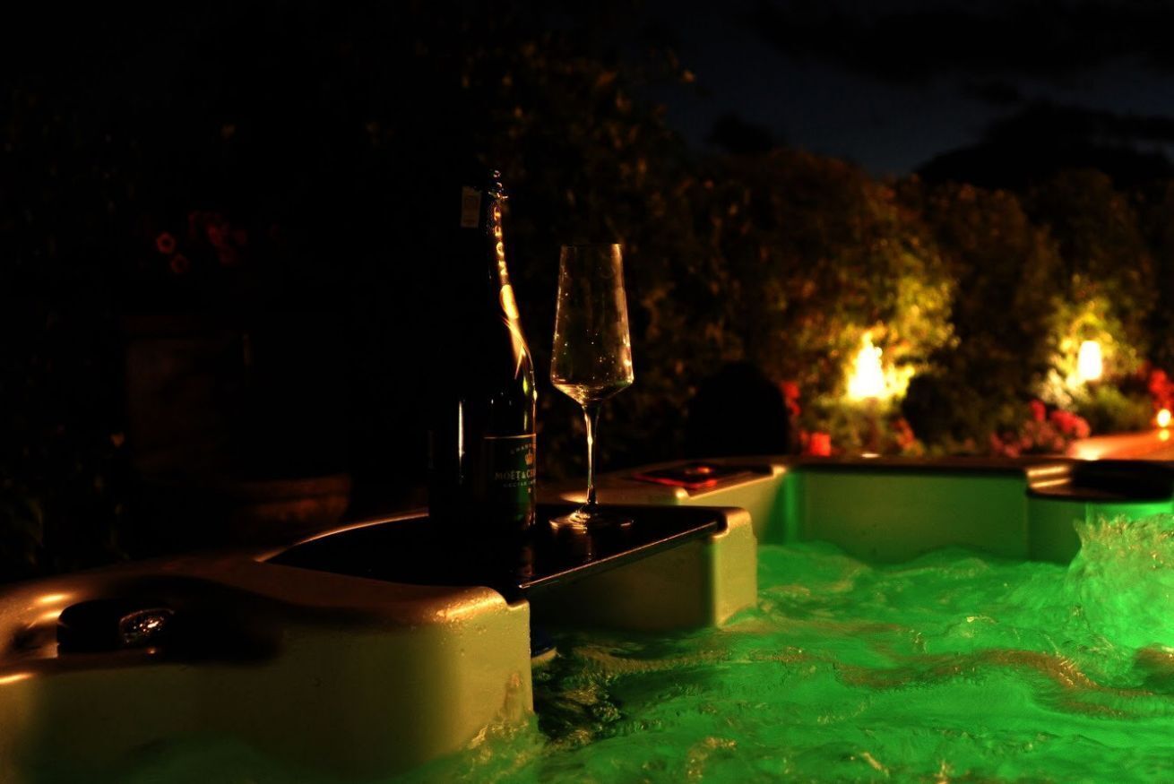 Een sfeervol verlichte eethoek buiten, met een tafel gedekt voor twee personen, inclusief een fles en een glas.