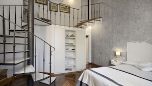 Ein Schlafzimmer mit einem Bett, einem Nachttisch, einer Lampe, einem Kleiderschrank mit Regalen und einer Wendeltreppe.