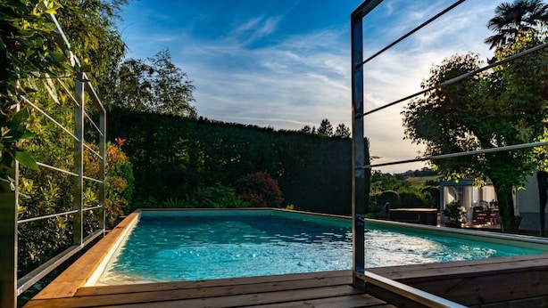 Ein rechteckiger Pool mit Holzterrasse, umgeben von üppigem Grün und blauem Himmel.