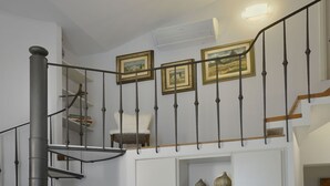 Eine Wendeltreppe mit Metallgeländer, ein weißer Stuhl und gerahmte Bilder an der Wand.