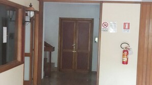 Un pasillo con piso de madera que lleva a una puerta cerrada. Hay señales de seguridad contra incendios y un extintor montado en la pared.