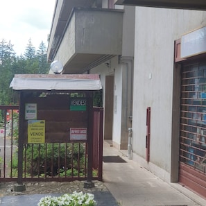 Ein Gebäudeeingang mit überdachter Wartezone, Schildern mit 'VENDESI' und 'AFFITTASI' sowie einem verschlossenen Auffahrtsweg.
