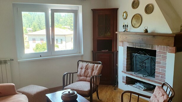 Una sala de estar con chimenea, muebles de madera y una ventana con vistas a un paisaje verde.