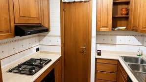 Una cocina compacta con armarios de madera, cocina a gas, horno empotrado, pileta y un estante pequeño con una olla de cerámica.