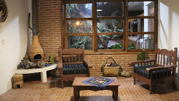 A cozy room with a brick wall, a large window, two wooden benches, a small table, and a decorative birdhouse. - Live like a local in San Cris! Pets welcome! (San Cristóbal de las Casas)